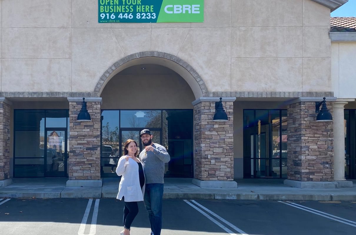 couple posing for a picture at a parking lot in front of a building