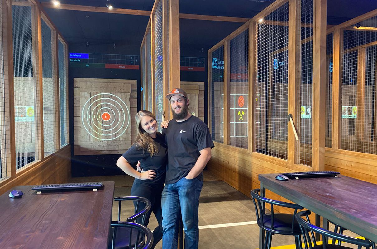young couple posing in front of axe throwing targets inside a bar