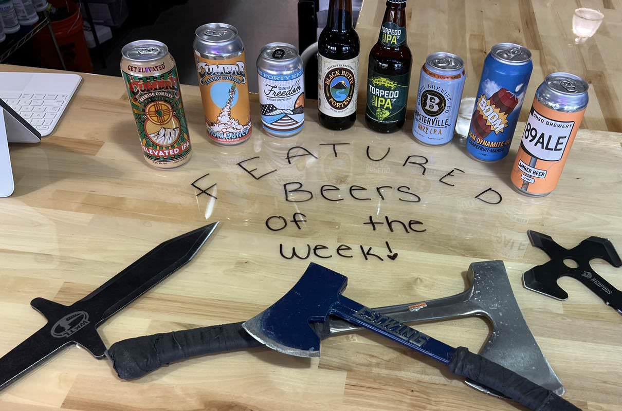 featured beers of the week at an axe throwing bar with a couple of axes and knives on the table