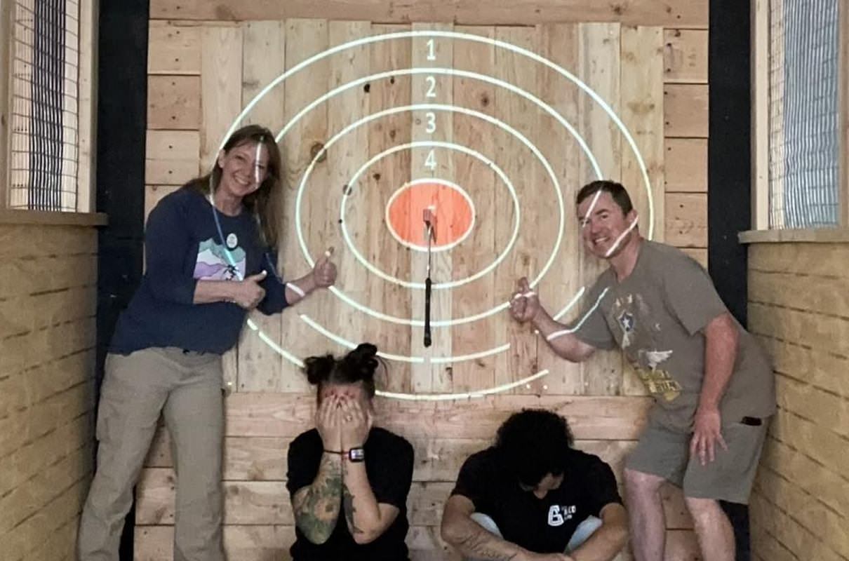 friends posing for a funny picture at an axe throwing bar with an axe stuck in the bullseye